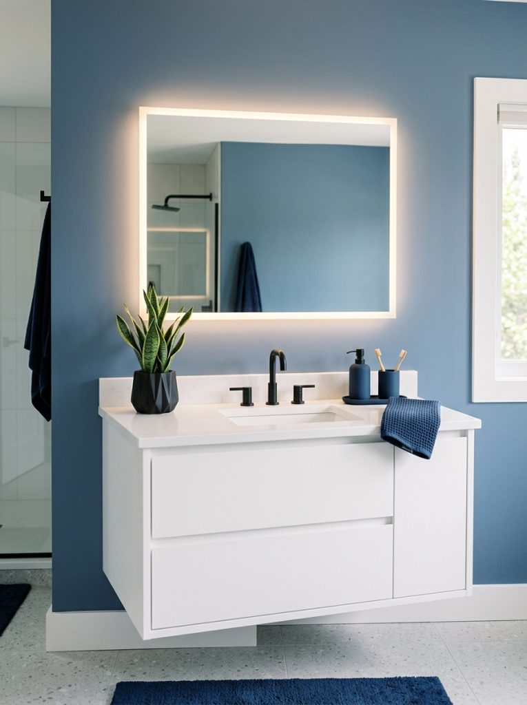 Modern blue bathroom aesthetic with slate blue walls backlit mirror floating white vanity black fixtures navy accessories and architectural plant