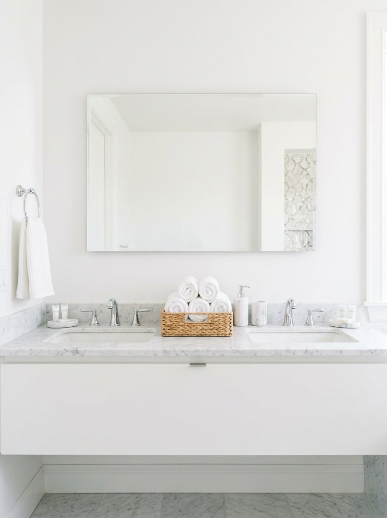 Hotel bathroom aesthetic with white walls frameless mirror rolled towels marble dispenser and bright even lighting