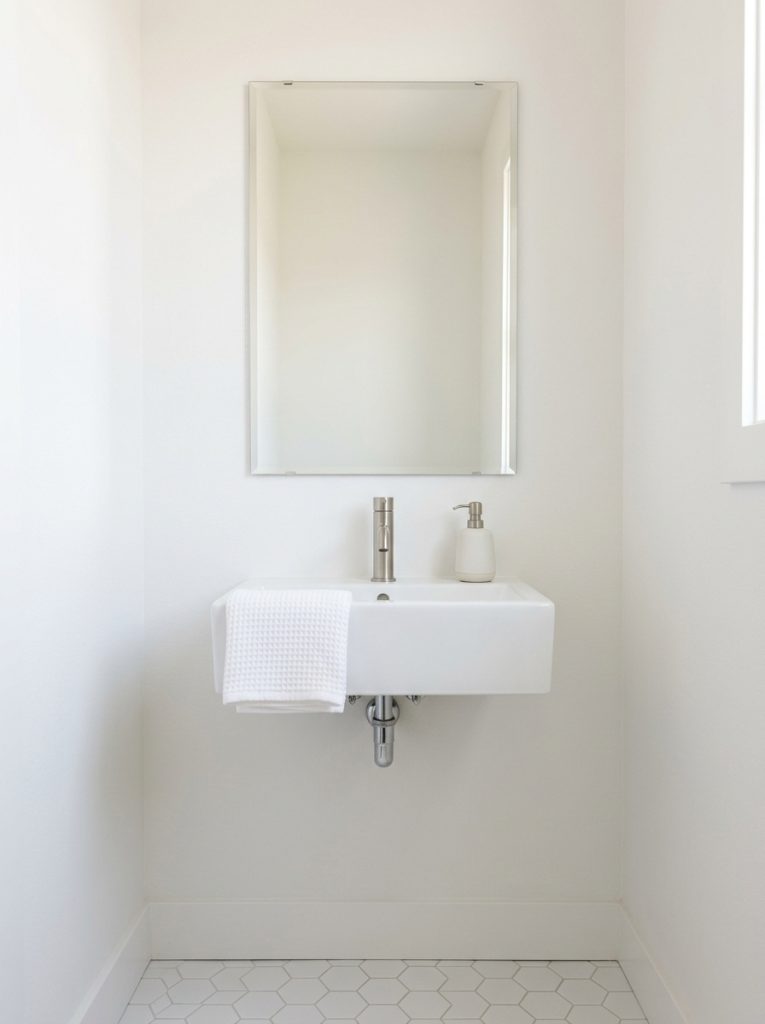  Minimalist guest half bathroom with white walls frameless mirror white sink ceramic dispenser and folded towel
