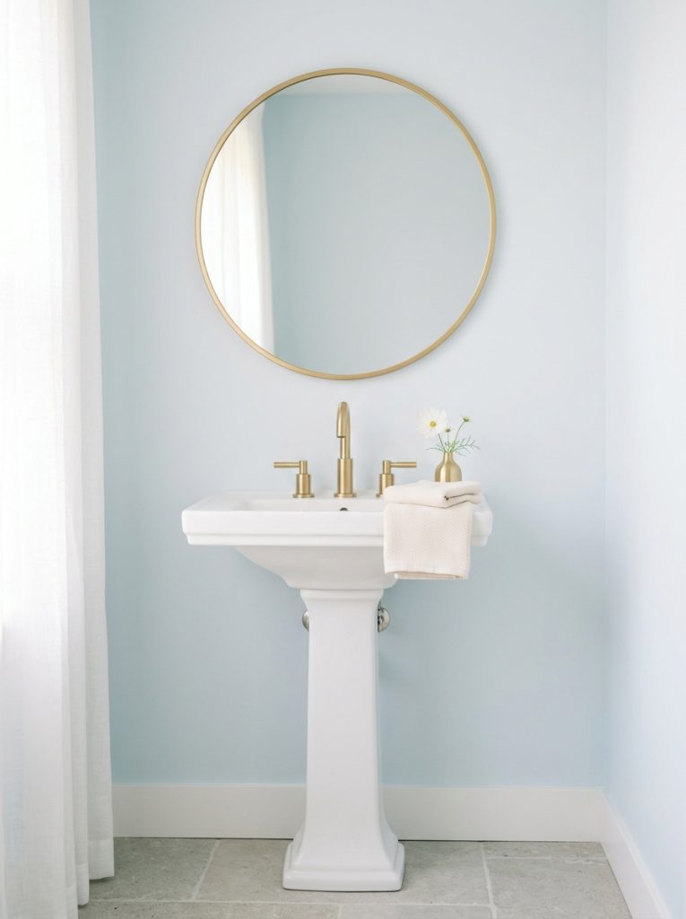 Powder blue bathroom aesthetic with powder blue walls gold mirror pedestal sink gold faucet cream towel and white flower in gold vase